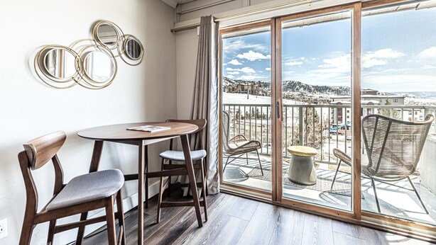 Ein Balkon mit Blick auf eine verschneite Landschaft, ein runder Tisch mit Stühlen und wandmontierte Spiegel.