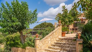 Un escalier en pierre mène à une terrasse dotée de sièges extérieurs, le tout étant entouré d’une végétation luxuriante et surplombé par un ciel dégagé.
