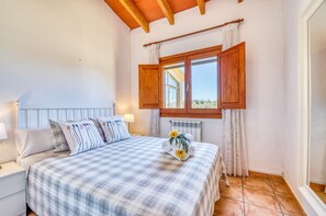 A bedroom with a bed, a nightstand, a window with wooden shutters, and a radiator. - Rural finca pool Es Sementaret in Mallorca (Arta)
