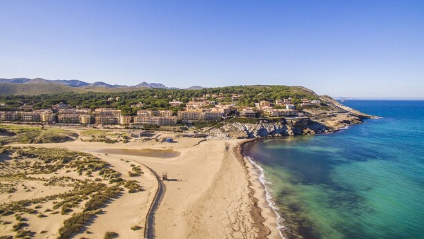 Une station balnéaire dotée de villas en bord de mer, d’une plage de sable et d’un paysage montagneux en arrière-plan.