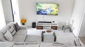 Un soggiorno moderno con un divano grigio, un tavolino da caffè con un modellino di nave, una TV a parete e un piccolo tavolino laterale.