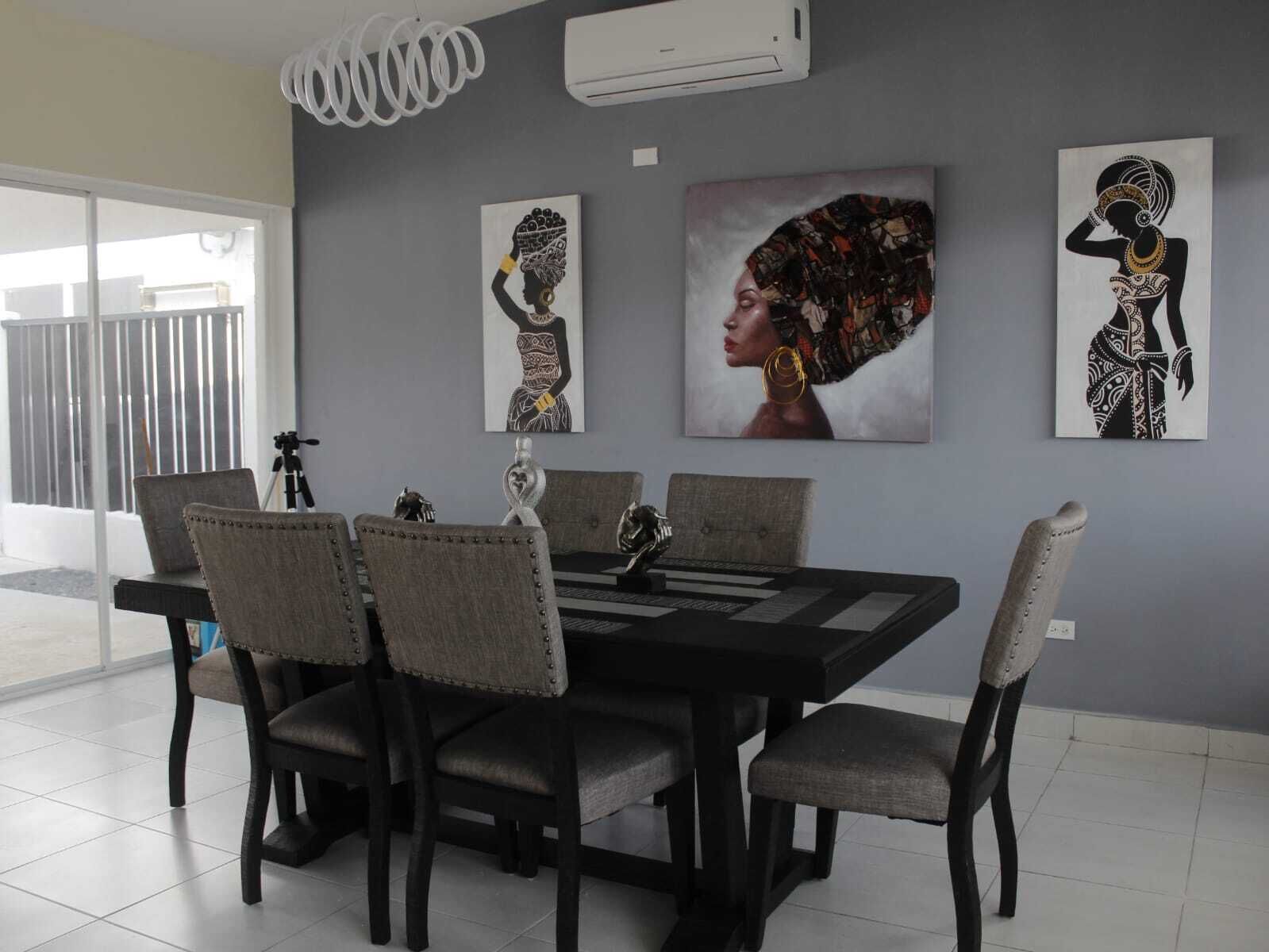 A dining area with a rectangular table, six chairs, and three artworks on the wall.