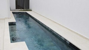 Una piscina stretta e rettangolare con acqua cristallina, circondata da pareti bianche e un solarium piastrellato.