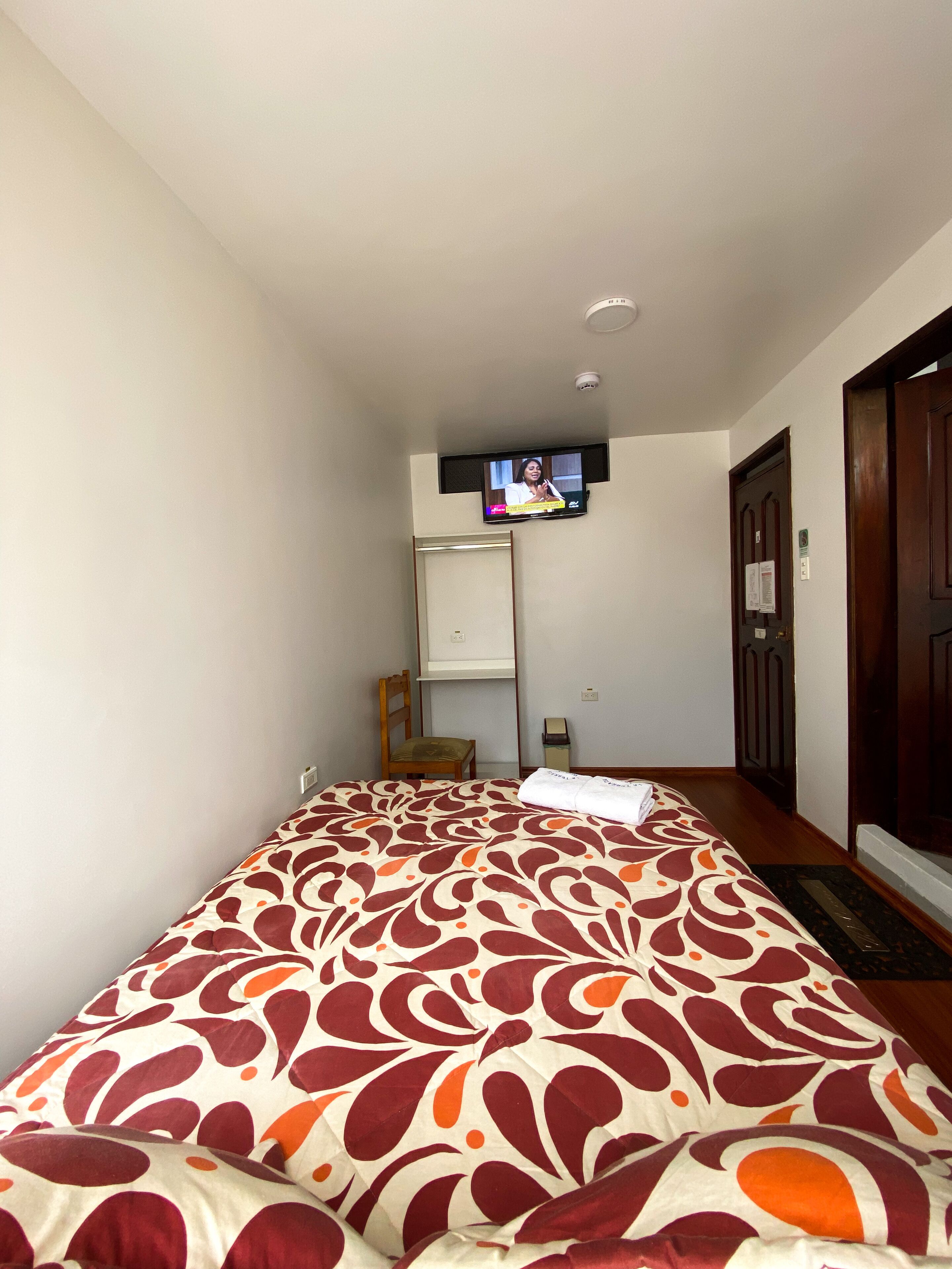 A hotel room with a bed, a television mounted on the wall, a chair, and a door.