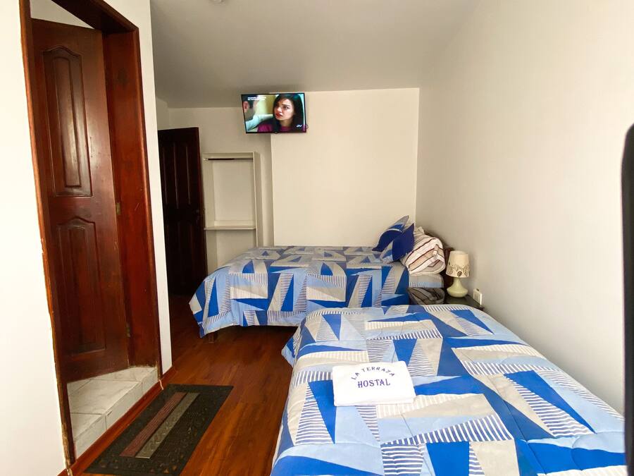 Habitación de hotel con dos camas, un televisor montado en la pared y una puerta que da a otra habitación.