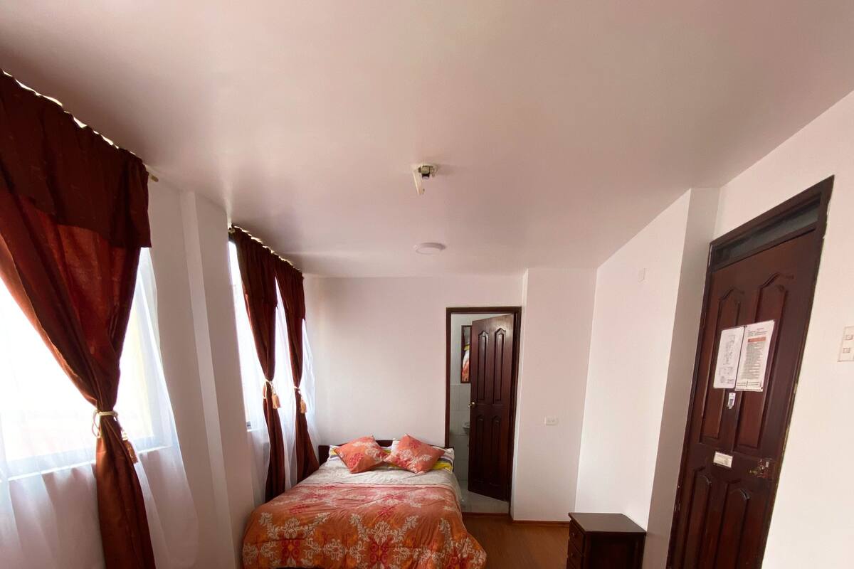 A hotel room with two beds, a wooden floor, a door with a sign, and a window with curtains.