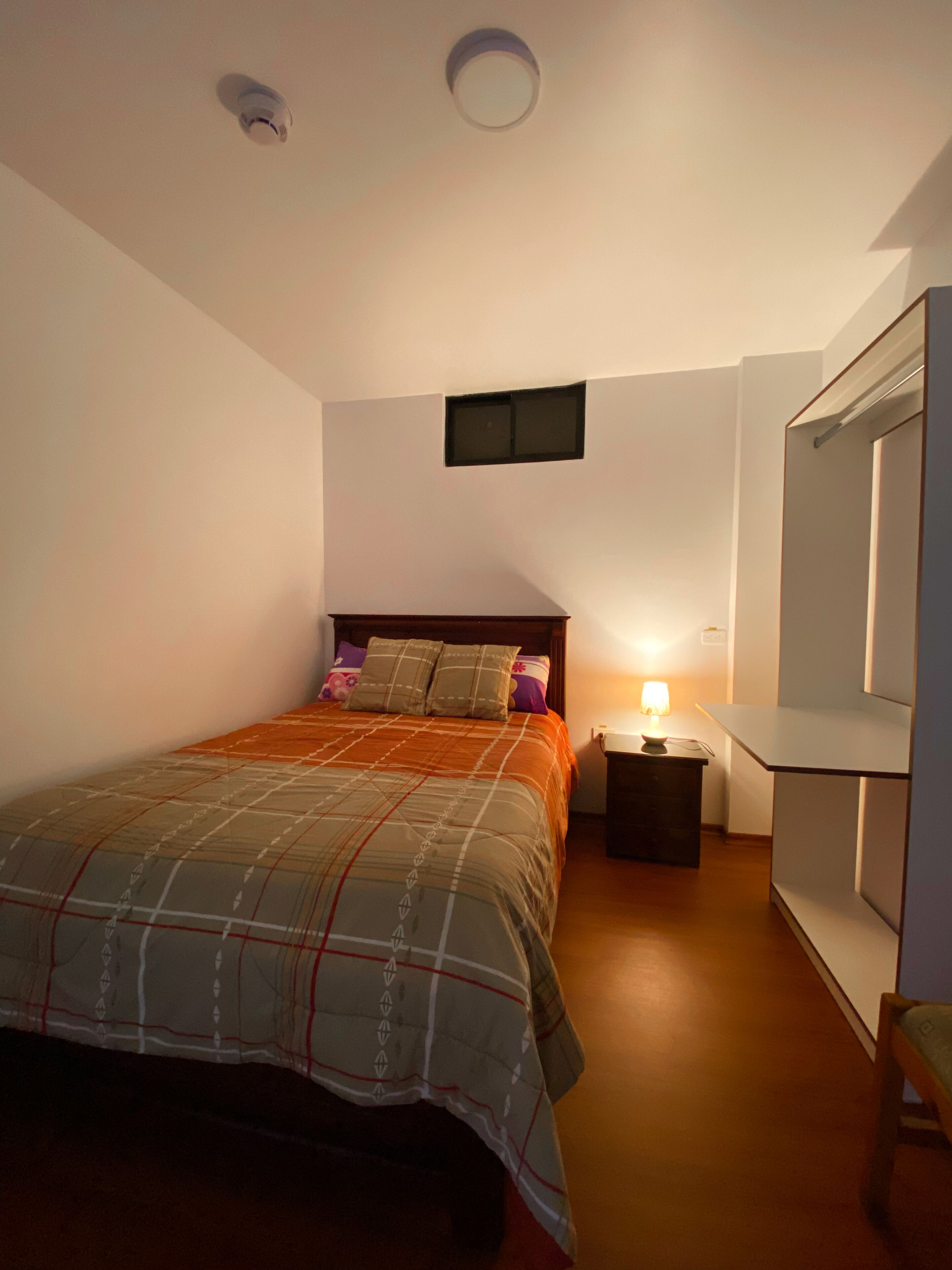 Ein Schlafzimmer mit Bett, Nachttisch, Lampe und Kleiderschrank.