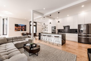 Enjoy a spacious living area with a comfortable sofa and coffee table, leading to a sleek kitchen with central island and bar stools.