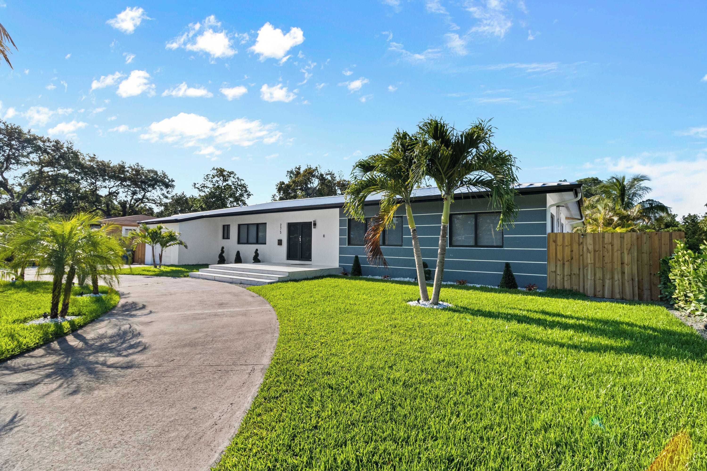 A modern two-story house with a paved driveway, a well-maintained lawn, and a wooden fence.