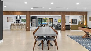 A spacious dining area with a long table and chairs, a kitchen in the background, and a pool table in the foreground.