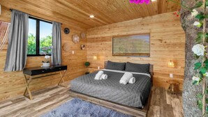 A wooden-paneled bedroom with a bed, a desk, and a window.