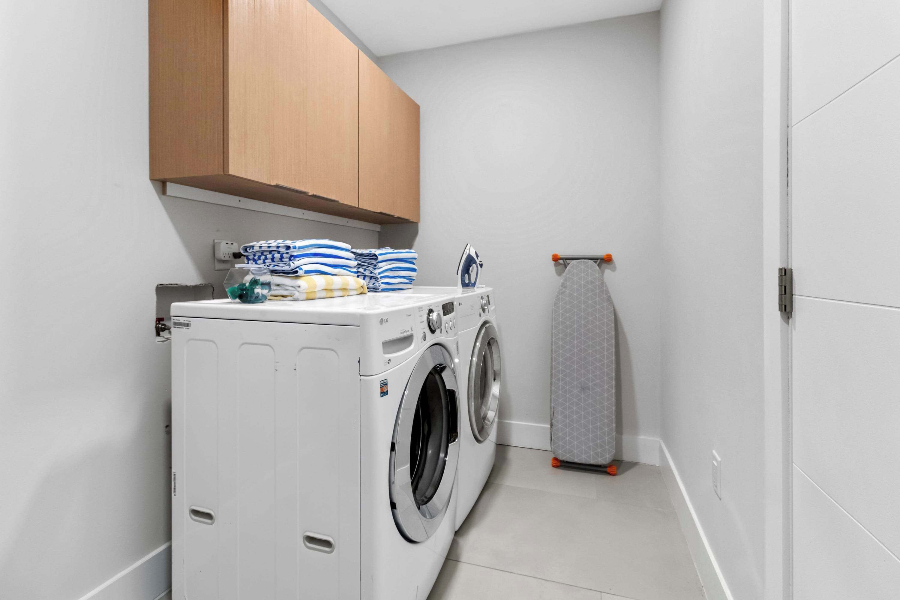 A laundry room with a front-loading washer and dryer, wooden cabinets, and a drying rack.