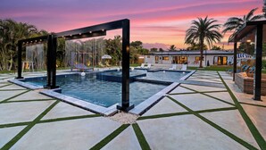 A swimming pool with a geometric tile pattern, a lounge area with chairs, and a sunset sky.