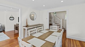 Un comedor amplio con una mesa de madera y sillas blancas, un espejo en la pared y una escalera que lleva a otra habitación.