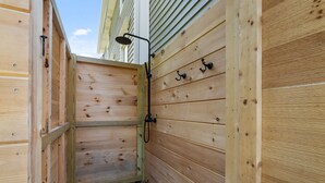 Un área de ducha exterior de madera con cabezal metálico y ganchos en la pared.