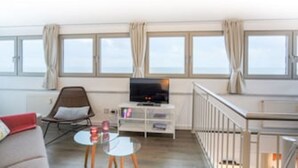 Hotellihuone, jossa on sohva, jalustalla oleva televisio, pieni pöytä ja parveke, jossa on kaide.