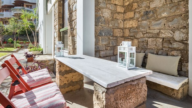 A stone wall, a white bench, and a wooden chair in a courtyard. - Glyfada 2 bedrooms 4 persons apartment by MPS (Γλυφάδα)