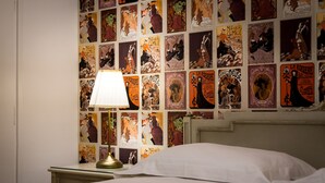 A hotel room with a bed, a nightstand with a lamp, and a wall decorated with vintage posters. - Glyfada 2 bedrooms 4 persons apartment by MPS (Γλυφάδα)