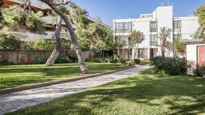 A courtyard with a paved walkway, surrounded by greenery and trees, leading to a modern building with balconies. - Glyfada 2 bedrooms 4 persons apartment by MPS (Γλυφάδα)