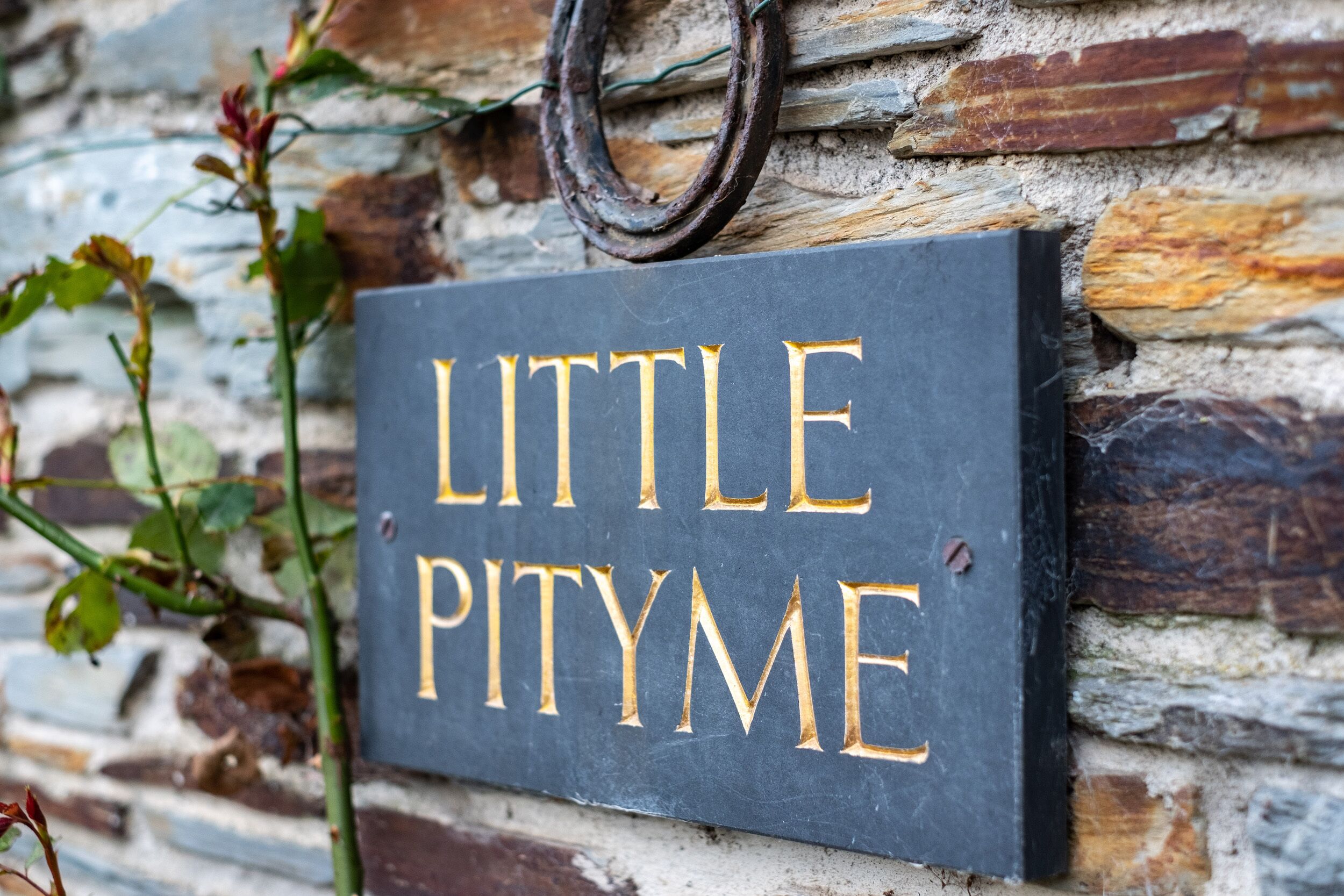 A slate sign with the words "LITTLE PITYME" mounted on a stone wall.