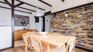 A dining area with a wooden table and woven chairs, a stone wall, and a ceiling with exposed beams.
