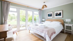 A bedroom with a large bed, a desk, and a view of the garden through the sliding doors.