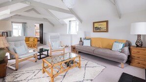 A spacious living room with high ceilings, a large window, a sofa, a chair, a coffee table, and a lamp.