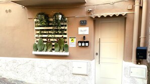 A building facade with a stone-paved entrance, a door, and a window with potted cacti. - Chianu Palì guest rooms (Agrigento)