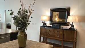 A kitchen with a granite countertop, a wooden cabinet with drawers, a vase with green foliage, and a mirror with a horse head decoration. - 2788 Horvat Lane (Wildwood)