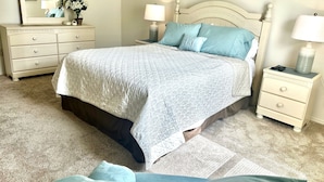Quarto com cama, mesas de cabeceira, cômoda, espelho e quadros na parede.