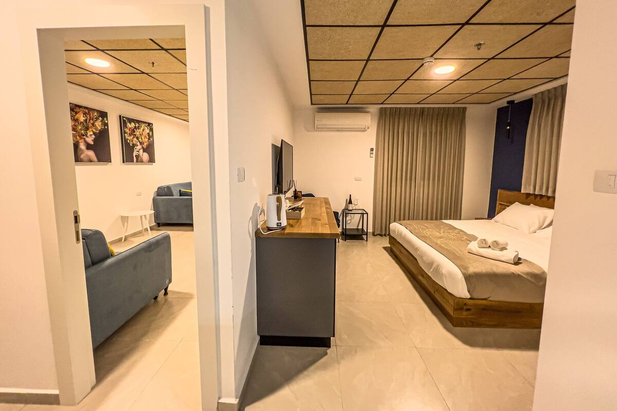 A modern hotel room with a bed, a desk, a chair, a flat-screen TV, and artwork on the walls.