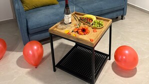 A room with a blue sofa, yellow cushions, a wooden coffee table with a bottle, glasses, fruit, and balloons.