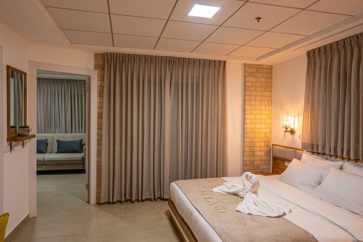 A hotel room with a large bed, a sofa, a mirror, and a brick accent wall.