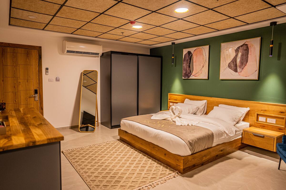 A modern bedroom with a wooden bed, a bedside table, a nightstand, a mirror, and artwork on the wall.