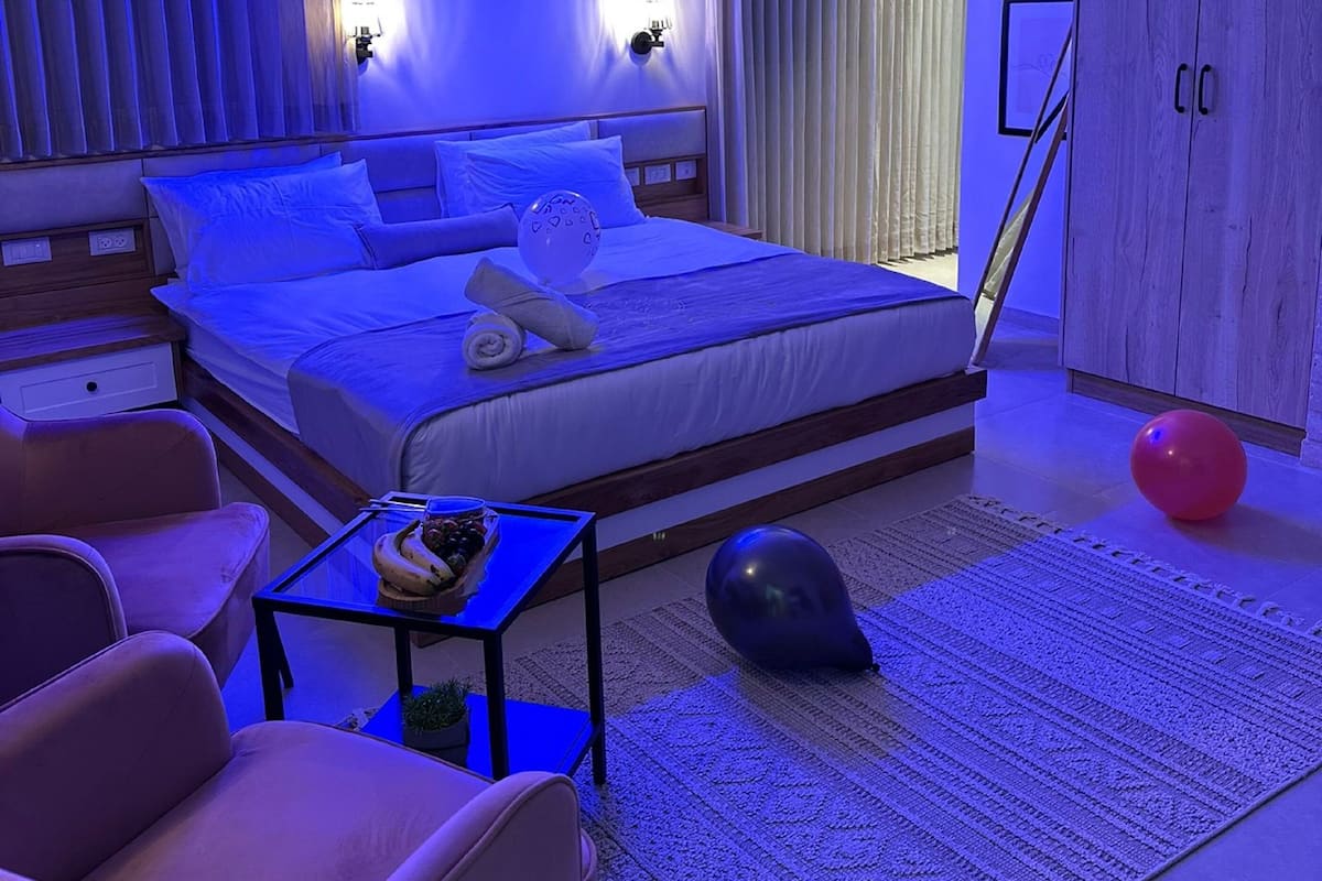 A modern bedroom with a large bed, a small table with a bowl of fruit, a red exercise ball, and a patterned rug.