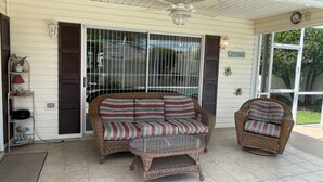 A covered porch with wicker furniture, including a sofa and a chair, and a glass table. - 441 Brentwood Ave (The Villages)