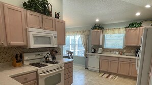 A kitchen with a stove, microwave, and dishwasher. There are cabinets, a sink, and a window with curtains. - 441 Brentwood Ave (The Villages)