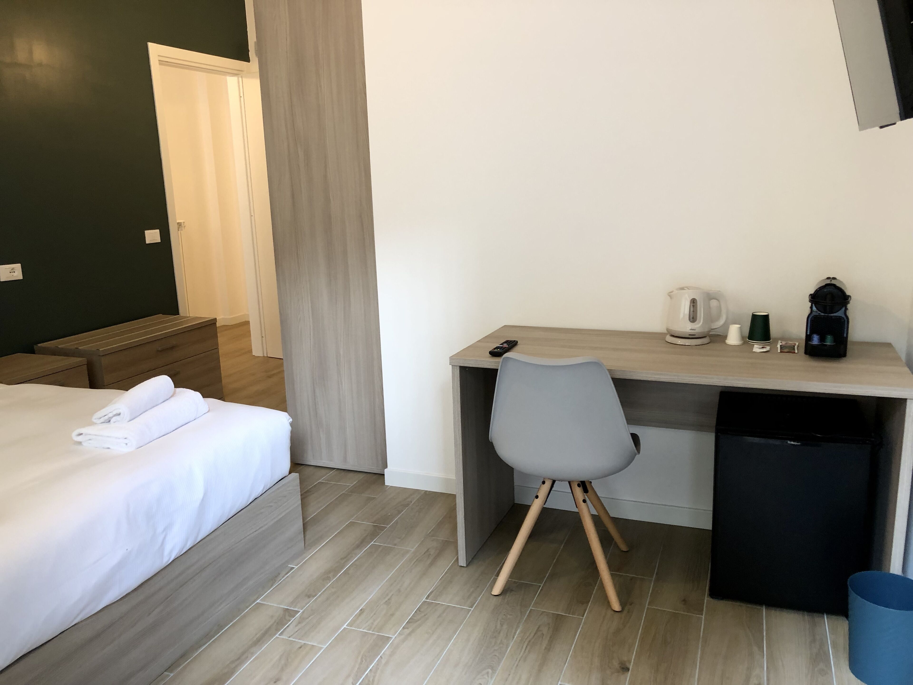 Una habitación de hotel con cama, escritorio, silla, cafetera y cesto de basura.