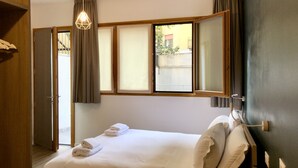 Una habitación de hotel con cama, ventana con cortinas, lámpara colgante y vistas al exterior.