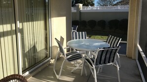 A covered patio with a round glass table and white metal chairs. - 1194 Flamingo Pl (The Villages)