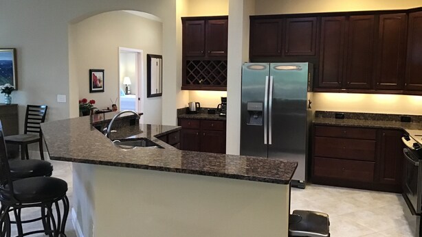 A modern kitchen with dark wood cabinets, a stainless steel refrigerator, granite countertops, and a built-in island with bar stools. - 1352 Kilgore Way (Wildwood)