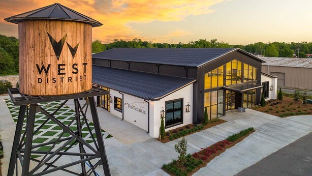 A modern building with a large wooden structure labeled "WEST DISTRICT" and a glass-fronted entrance. - Freedom's Flight - The Post Lofts (Statesboro)
