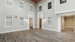 A spacious interior with white walls, multiple windows, and a wooden floor. - Freedom's Flight - The Post Lofts (Statesboro)