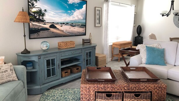 A living room with a large TV, wicker furniture, a white sofa, and a patterned rug. - 5597 Sharpin St (Wildwood)
