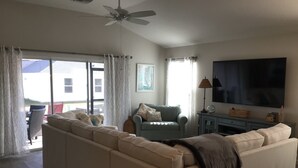 A spacious living room with a large sofa, a television, and a ceiling fan. - 5597 Sharpin St (Wildwood)