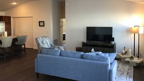 Een woonkamer met een bank, een televisie, een plafondventilator en een eethoek met stoelen en een tafel.