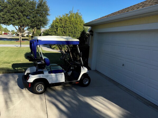 A golf cart parked in a driveway next to a garage. - 890 Chappells Dr (The Villages)