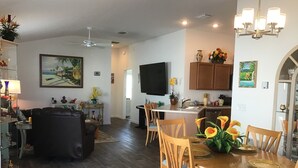 A spacious living area with a dining table set for four, a kitchen with wooden cabinets, and a flat-screen TV mounted on the wall. - 2454 Lewis Ln (Wildwood)