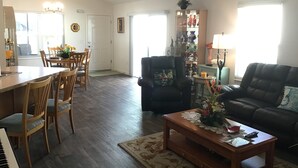 A spacious living room with a piano, a dining area with wooden chairs, a black leather sofa, and a coffee table with a vase. - 2454 Lewis Ln (Wildwood)