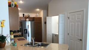 A kitchen with a granite countertop, stainless steel sink, and a refrigerator. There are two wooden chairs and a potted plant. - 2454 Lewis Ln (Wildwood)